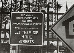 Sign affixed to a park fence saying "NYC OWNS 30,000 EMPTY APTS - AND HAS 30,000 HOMELESS PEOPLE - NYC's COST EFFECTIVE SOLUTION: LET THEM DIE IN THE STREETS"